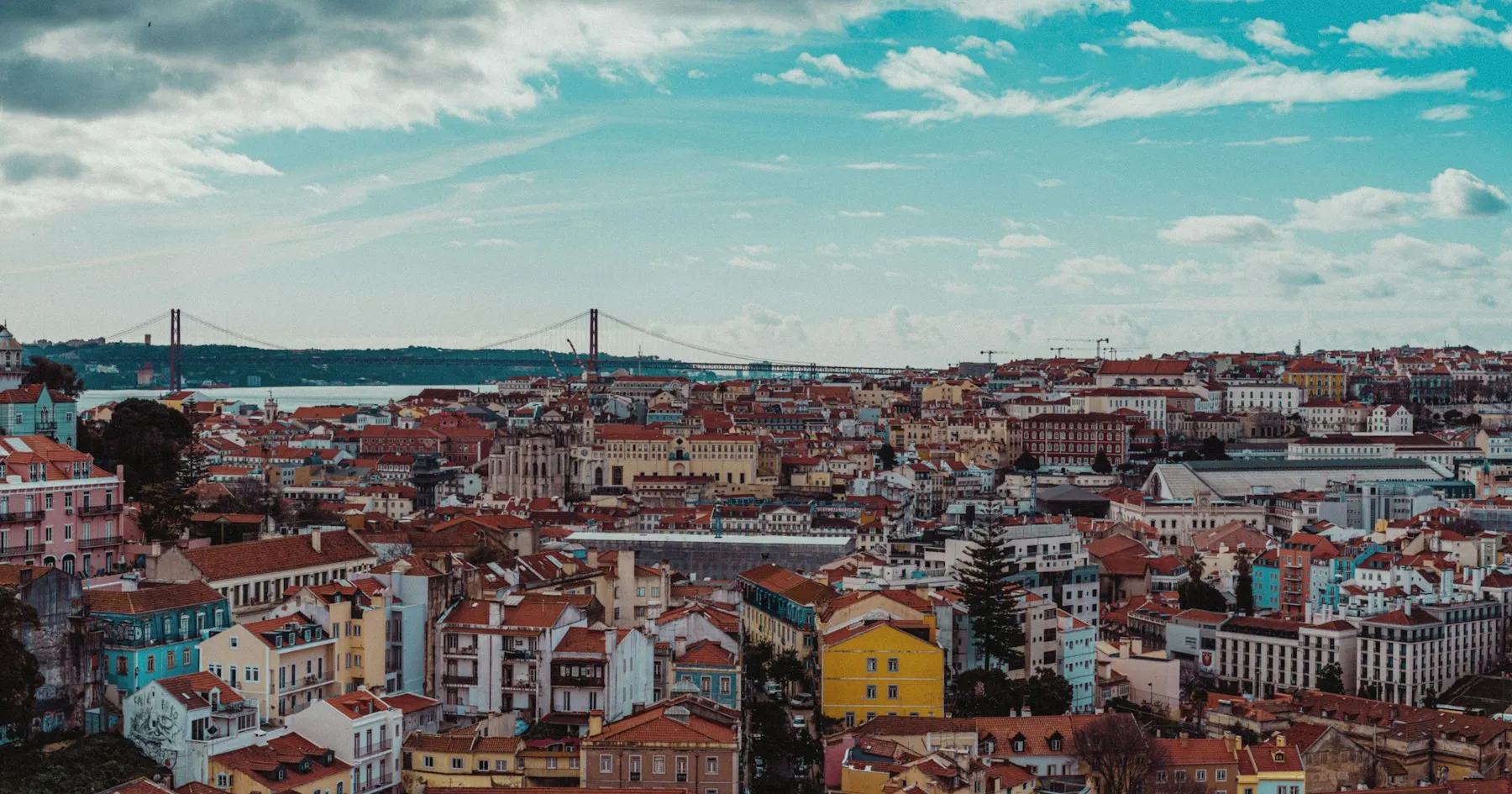 Colourful Lisbon homes and terracotta rooftops overlooking the Tagus River and suspension bridge